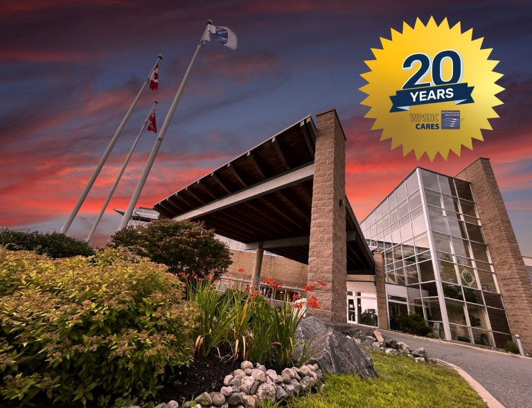 West Parry Sound Health Centre’s main entrance looms large in front of the viewer, as flags wave in the breeze. In the background a vivid sunset fills the sky. Superimposed on the image in the corner is a badge celebrating 20 years and the WPSHC Cares logo.
