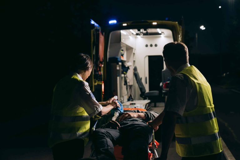 Paramedics assist an injured person in front of an ambulance.