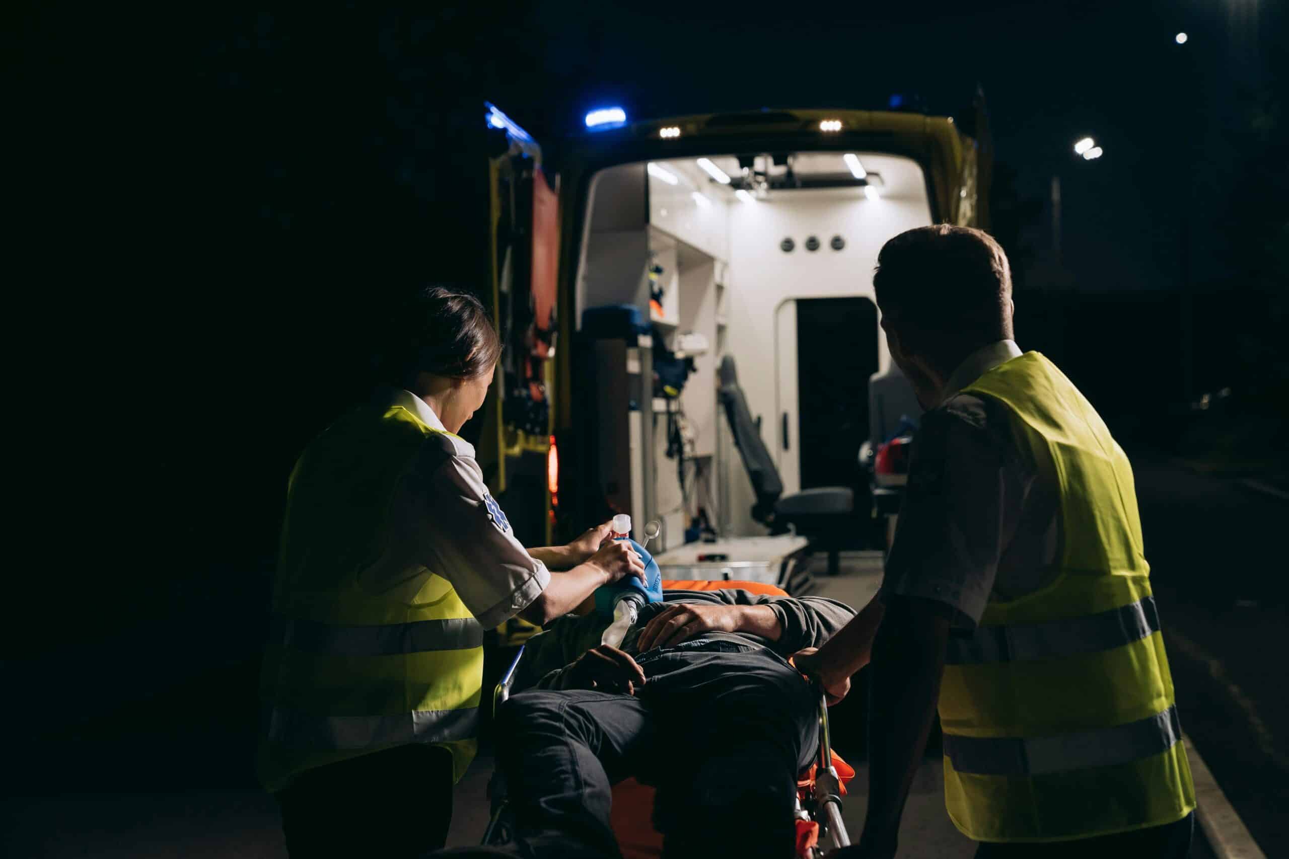 Paramedics assist an injured person in front of an ambulance.